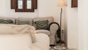 A room with a sofa set, a floor lamp, and a window with wooden shutters.