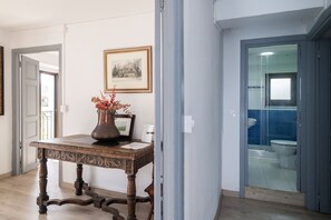 Een kamer met een houten tafel, een vaas met gedroogde bloemen, een lijst met een foto en een badkamer met een blauwe betegelde muur en een toilet.