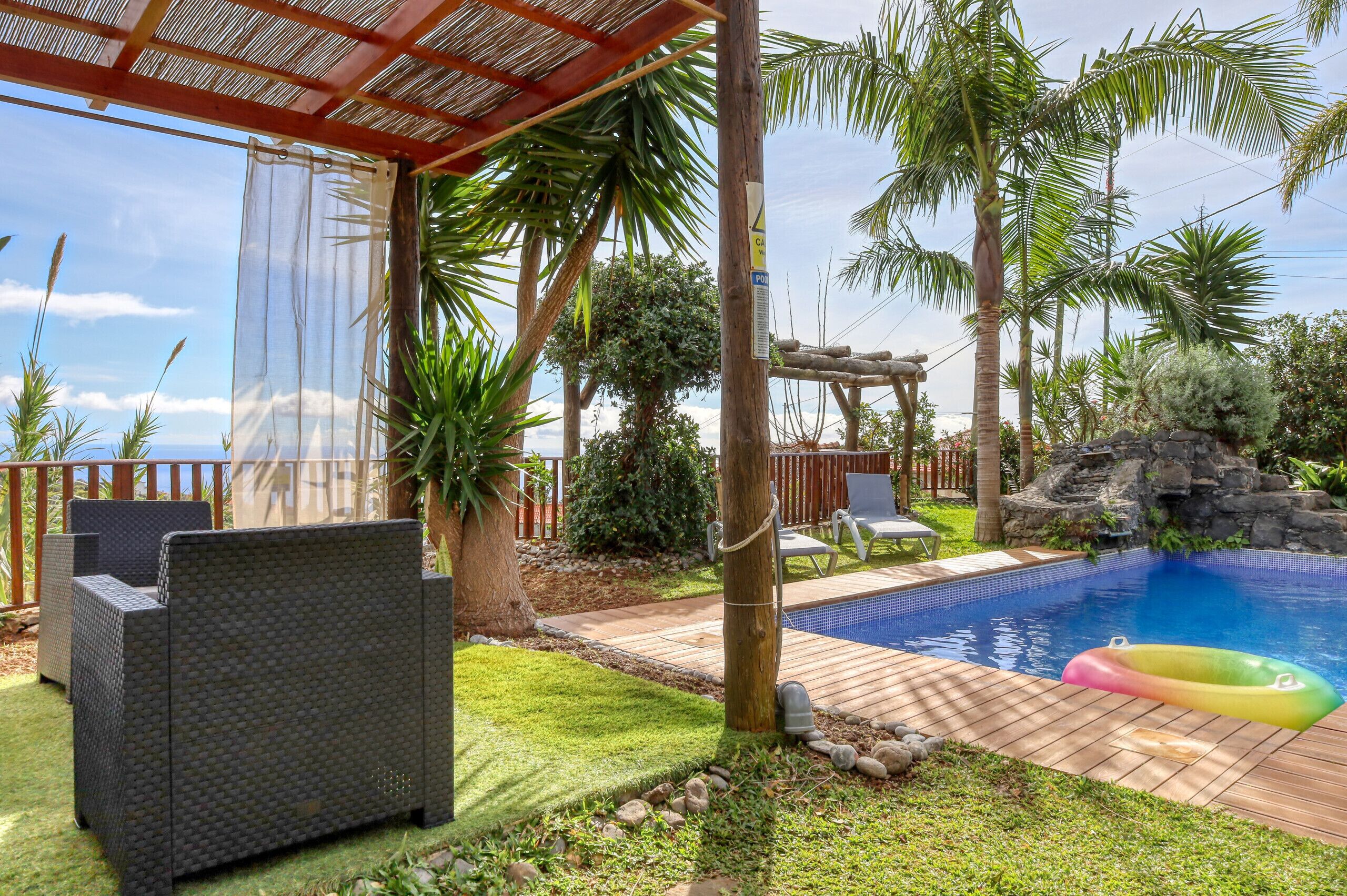 Un patio trasero con piscina, mobiliario exterior y una pérgola.