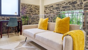 A cozy living area with a beige sofa, yellow cushions, a desk with a chair, and a stone wall. - Ricardo House, a Home in Madeira (Calheta)