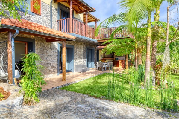 Un bâtiment en pierre doté d’un balcon, d’un patio et d’un jardin luxuriant.