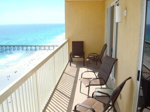 A balcony with a view of the beach and pier, featuring two chairs and a table.