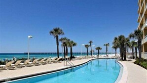 A swimming pool with lounge chairs and palm trees, overlooking a beach and pier.
