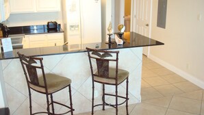 A kitchen with white cabinets, a black countertop, and two wooden bar stools.