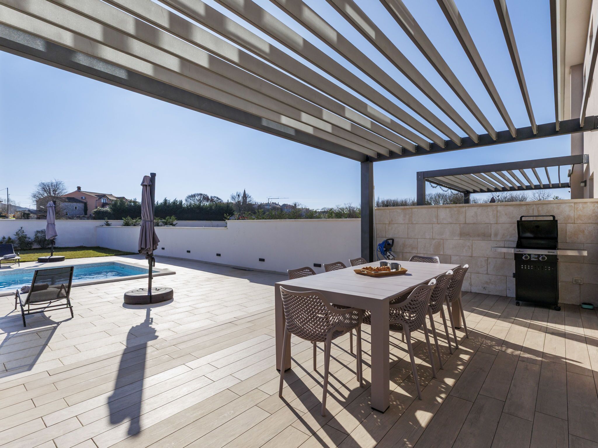 Une terrasse extérieure avec une piscine, une table et des chaises, ainsi qu’un barbecue.