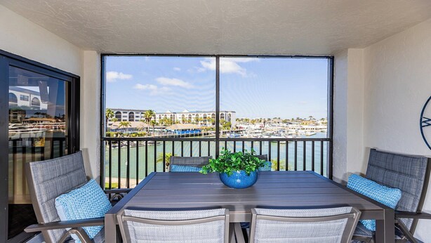 Un balcon avec une table et des chaises, un pot de fleurs et une vue sur un port de plaisance et des immeubles.