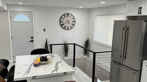 A modern kitchen with a marble countertop, stainless steel appliances, and a black-framed clock on the wall.