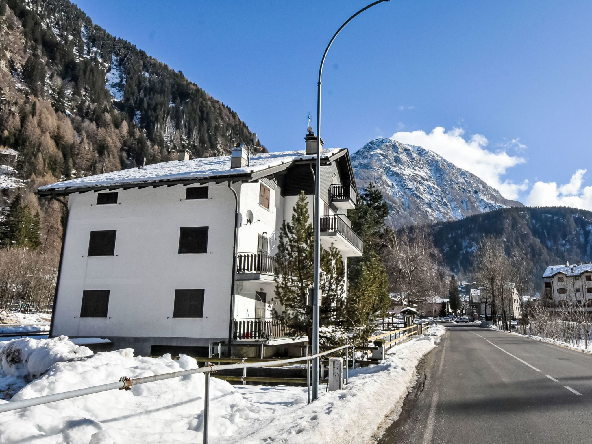 Ein zweistöckiges Gebäude mit Balkonen, einem mit Schnee bedeckten Dach und einer Bergkulisse.