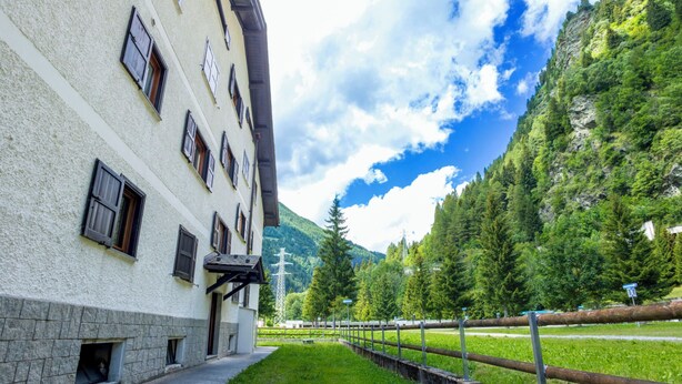 A building with multiple windows and a balcony, surrounded by a grassy area and a mountain backdrop. - Leonardi Terrace by Interhome (Campodolcino)