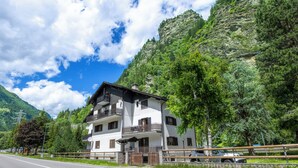 A two-story building with balconies, a paved road in front, and a mountainous backdrop. - Leonardi Terrace by Interhome (Campodolcino)