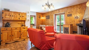 A cozy room with wooden walls, a dining table with chairs, a fireplace, and a kitchen area with cabinets and a kettle. - Leonardi Terrace by Interhome (Campodolcino)
