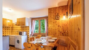 A compact kitchen with wooden cabinets, a washing machine, and a dining area with a wooden table and chairs. - Leonardi Terrace by Interhome (Campodolcino)