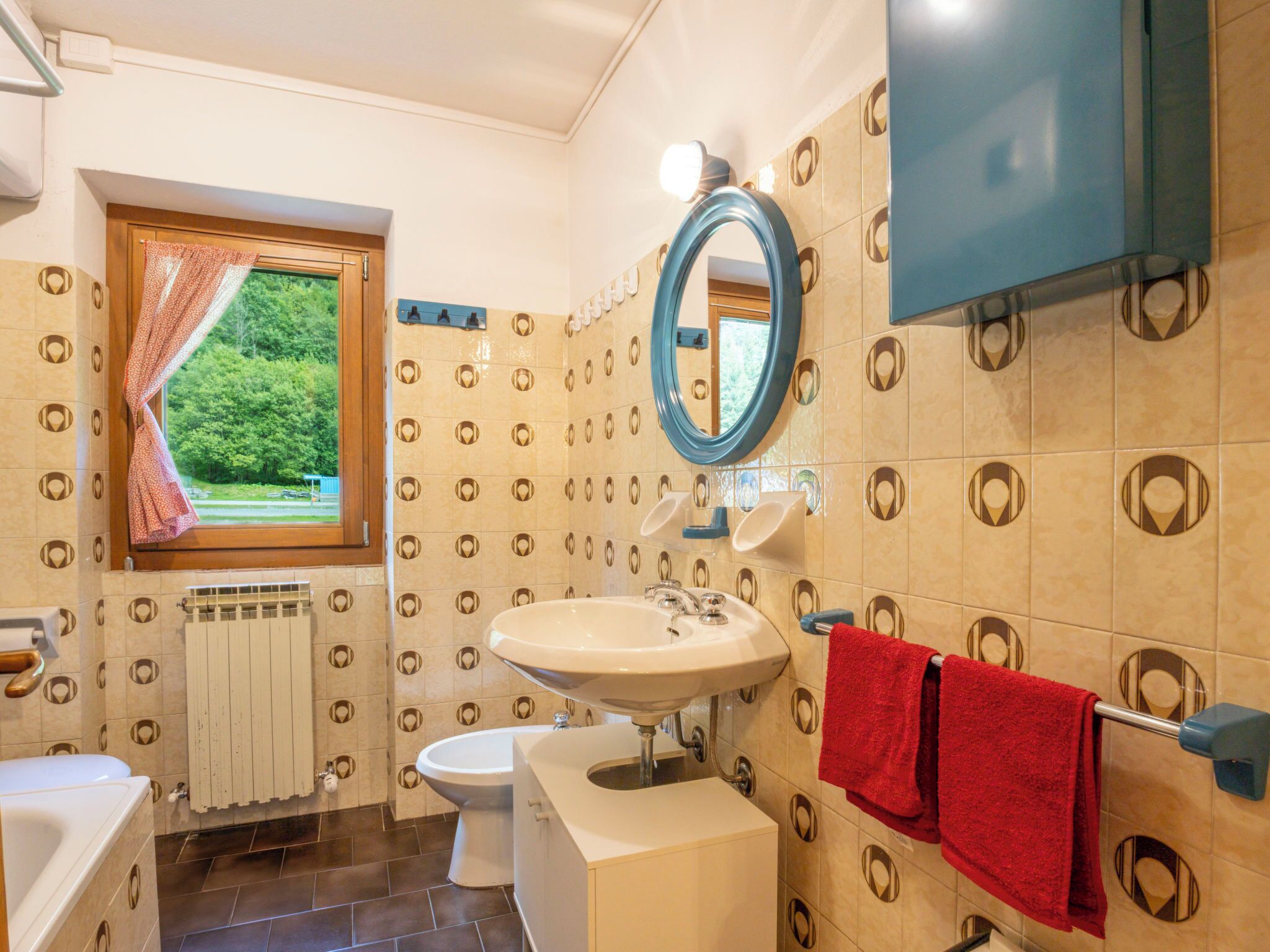 Ein Badezimmer mit Waschbecken, Toilette und Badewanne. Ein Fenster bietet Blick auf grüne Landschaft.