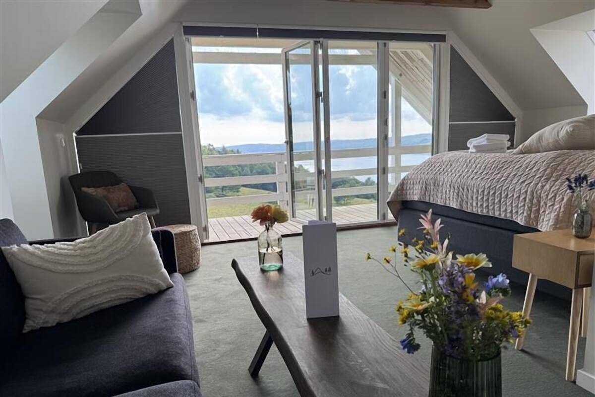 Une chambre moderne avec une grande fenêtre, un lit, un canapé et une table agrémentée de fleurs.