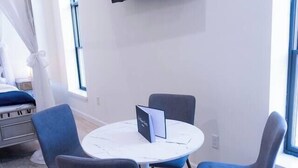 A modern room with a round table, two chairs, a flat-screen TV mounted on the wall, and a bed with a canopy. - Royal Suite Modern Studio Downtown on the Square (Bloomington)