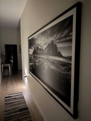 A hallway with a framed black and white landscape painting on the wall, a wooden floor, and a rug. - Royal Suite Modern Studio Downtown on the Square (Bloomington)
