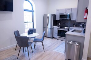 A modern kitchen with stainless steel appliances, a dining area with a round table and chairs, and a large window providing natural light. - Royal Suite Modern Studio Downtown on the Square (Bloomington)