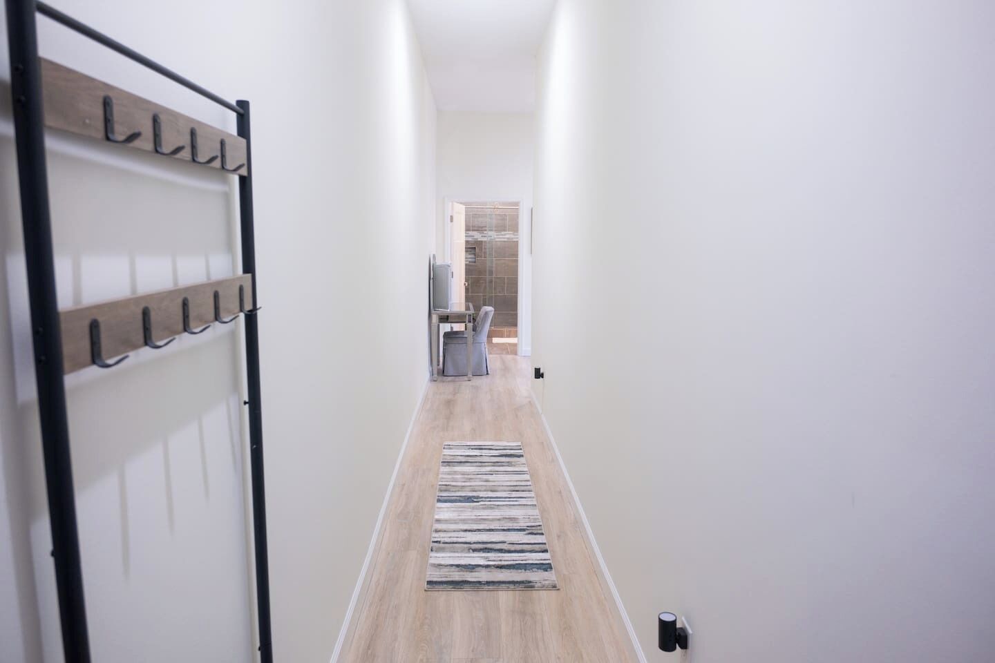 Un pasillo con perchero, un escritorio con silla y un área de ducha con azulejos.