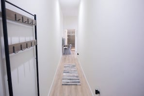 Un pasillo con perchero, un escritorio con silla y un área de ducha con azulejos.