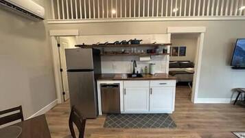 A compact kitchen with a refrigerator, a sink, and a dishwasher. There is a small dining area with a table and chairs. The kitchen has a modern design with white cabinets and a wooden countertop.