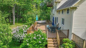 A deck with outdoor furniture, surrounded by lush greenery and flowering plants. - 4 BDR w/ Private Hot tub, Backyard and Deck! (Wells)