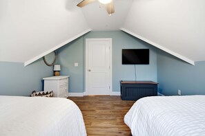 A bedroom with two beds, a TV, a white door, and a ceiling fan. - Maritime Meadows – Charming Resort-Style Home! (Arundel)