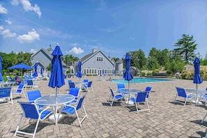 Ein Poolbereich mit blauen Sonnenschirmen, Liegestühlen und einem Haus im Hintergrund.