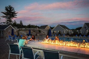 Un espace aménagé au bord de la piscine, doté d’un foyer, de sièges extérieurs et offrant une vue sur la piscine et les bâtiments environnants.