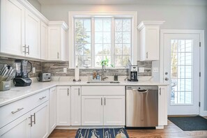 A modern kitchen with white cabinets, a built-in stove, a coffee maker, and a dishwasher.