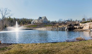 A large house with a stone retaining wall and a pond with a fountain.