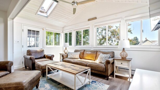 A sunlit room with a ceiling fan, a sofa, a coffee table, and a lamp. - Near Crescent + Wells Beach • Firepit • Sleeps 10 (Wells)