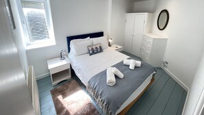 A modern bedroom with a bed, nightstands, a wardrobe, and a window.
