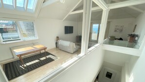A spacious loft bedroom with a large window, a wooden table, a striped sofa, and a view of the outdoors.