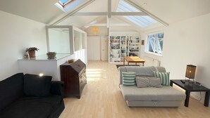 A spacious living room with a high ceiling, skylights, a large bookshelf, a sofa, and a coffee table.