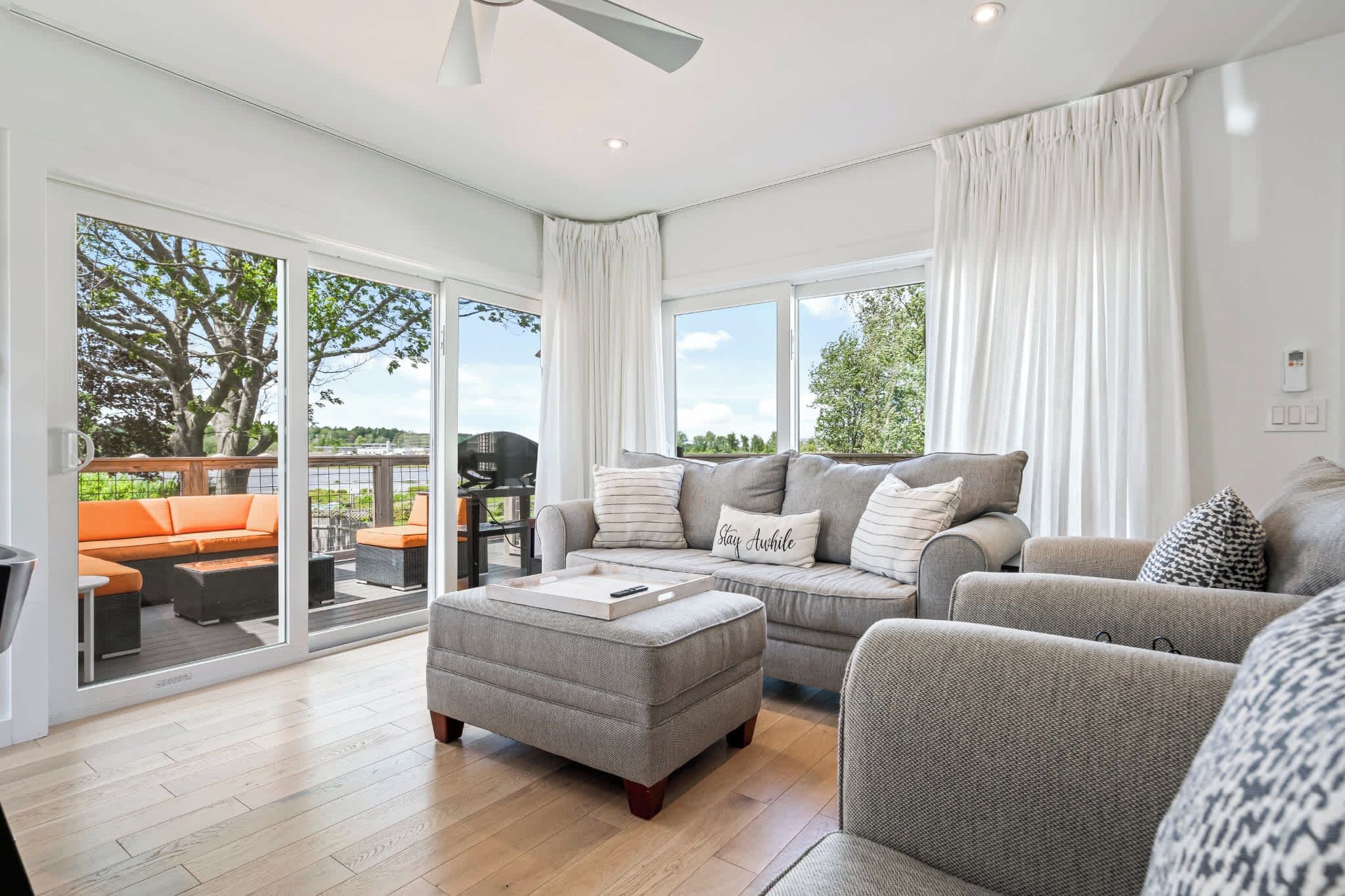 A spacious living room with a grey sofa set, a grey ottoman, and a large sliding glass door leading to an outdoor patio.