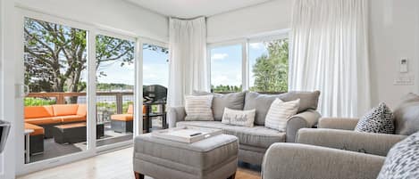 A spacious living room with a grey sofa set, a grey ottoman, and a large sliding glass door leading to an outdoor patio.