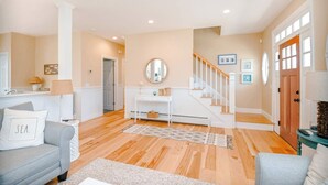 A spacious living room with hardwood flooring, a grey sofa, a white console table, and a staircase leading to another level. - Stunning 5 BDR, Walk to York Harbor Beach! (York)