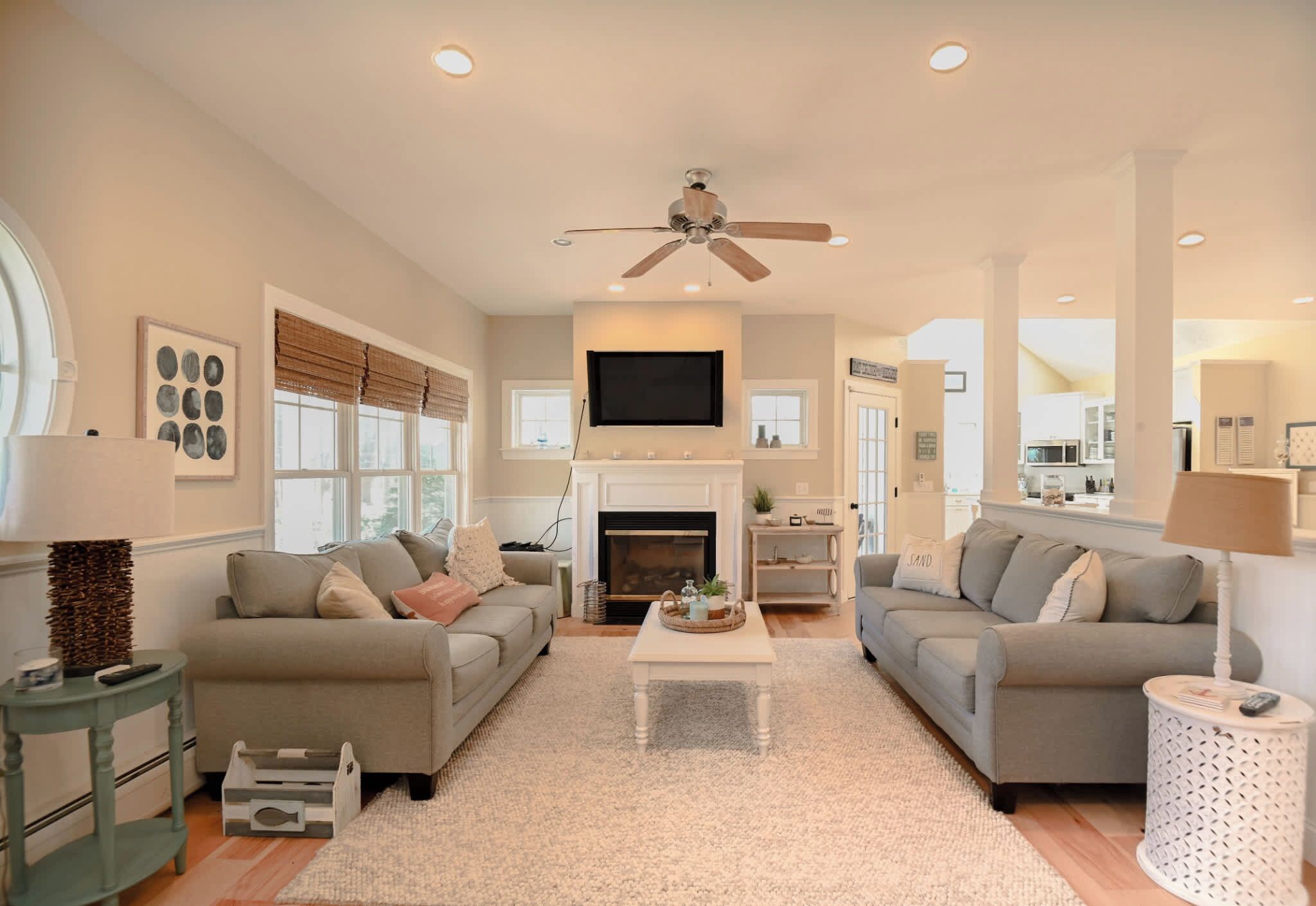 A living room with two sofas, a fireplace, a ceiling fan, and a television mounted above the fireplace.
