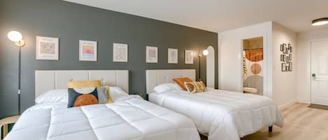 Hotellihuone, jossa on kaksi sänkyä, harmaa seinä ja kehystetty taideteos.