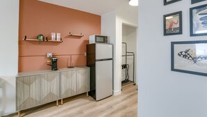 A kitchenette with a microwave, refrigerator, and a coffee machine on a cabinet. There are framed pictures on the wall and a shelf with cups and a plant. - 5 min. to Lincoln's top attractions. Two-queens beds, pickleball & outdoor space (Lincoln)