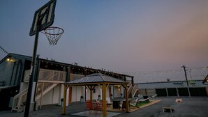 Een buitenbasketbalveld met een ring, een overdekt zitgedeelte en lichtslingers.