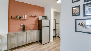 Een kitchenette met een koelkast, magnetron en koffiezetapparaat op een kast.
