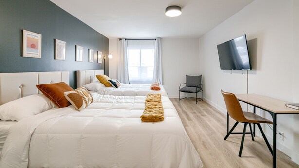A hotel room with two beds, a desk, a chair, a TV, and framed pictures on the wall. - 5 min. to Lincoln's top attractions. Two-queens beds, pickleball & outdoor space (Lincoln)