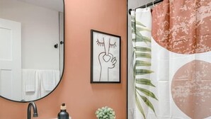 Een badkamer met een witte wasbak, een spiegel, een toilet, een douchegordijn en een lijst met een foto aan de muur.