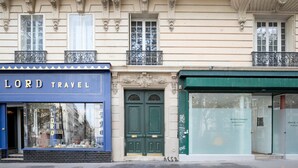 A building facade with a blue storefront labeled "LORD TRAVEL" and a green door. - Blueground | République, concierge, courtyard view (Paris)