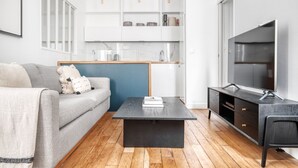 A modern living room with a grey sofa, a black coffee table, and a TV on a stand. - Blueground | République, concierge, courtyard view (Paris)