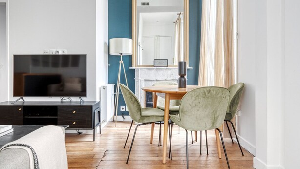 A modern living room with a flat-screen TV, a dining table with chairs, a large mirror, and a floor lamp. - Blueground | République, concierge, courtyard view (Paris)