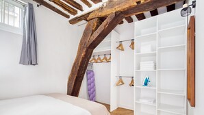 A bedroom with a wooden ceiling, a bed, a wardrobe, and a window with a curtain. - Blueground | Ile Saint Louis, nr Notre Dame (Paris)