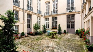 A courtyard with a cobblestone floor, surrounded by buildings with balconies and windows. - Blueground | Ile Saint Louis, nr Notre Dame (Paris)