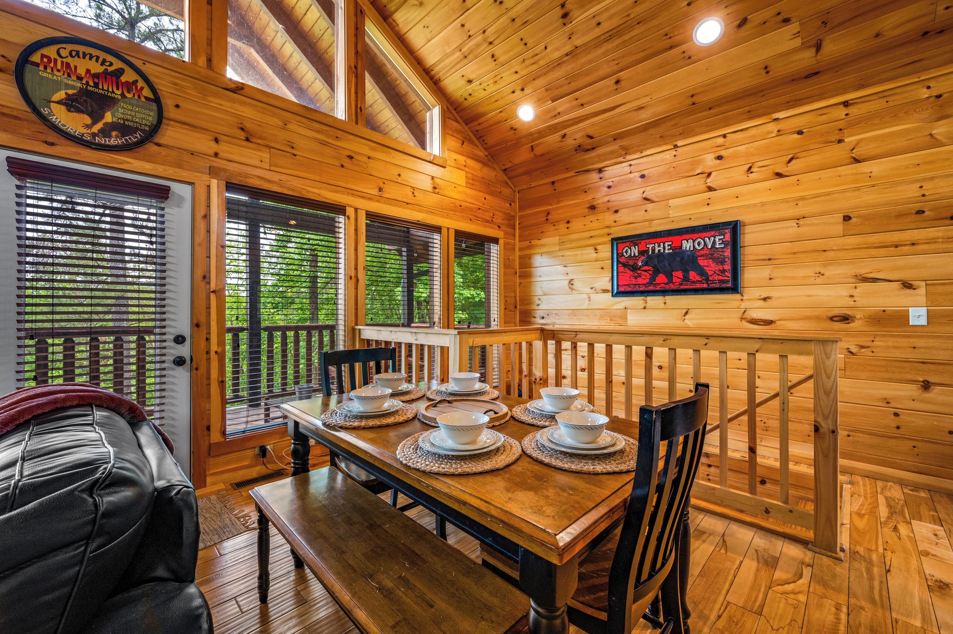 Interior de una cabaña de madera con una mesa de comedor preparada para seis personas, un sofá de cuero y un letrero que dice 'Camp Run-A-Muck'.